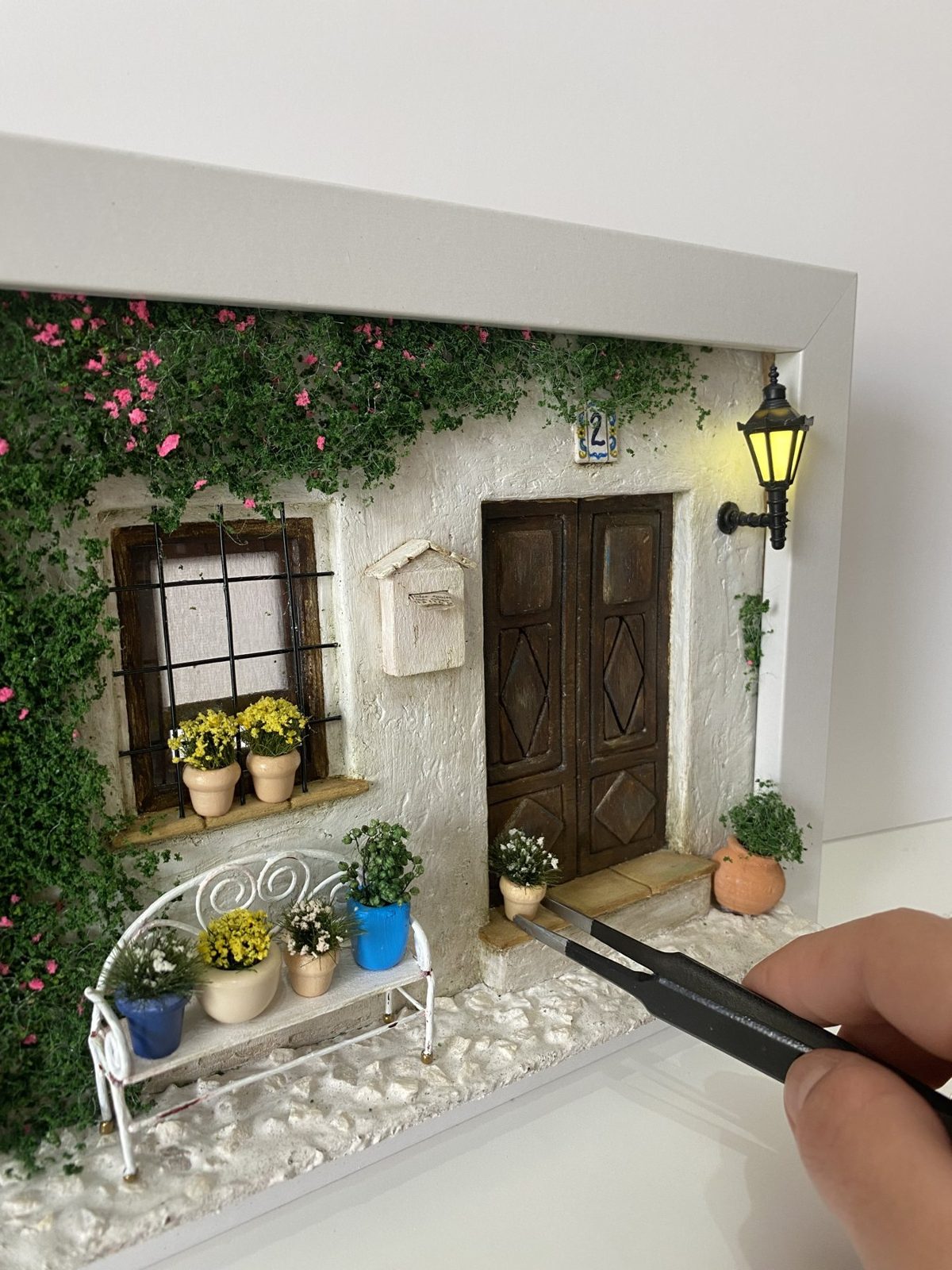 White courtyard wall with bougainvillea, a bench and a lit lantern