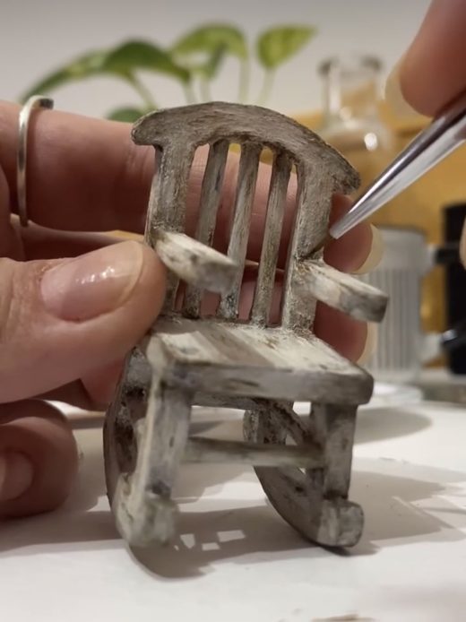 Weathered miniature rocking chair being painted with tweezers