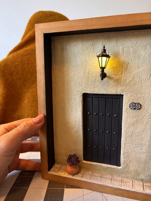 Cream wall with a black door, number 303, and a lit lantern